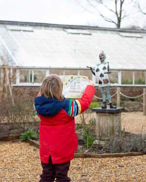 A child reading a Trail Map at Forde Abbey, stood in front of a bronze Knave sculpture by Robert James Workshop