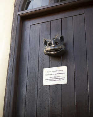 The front door of the Robert James Workshop Gallery with the Cheshire Cat Face Sculpture attached and an appointment-only sign below