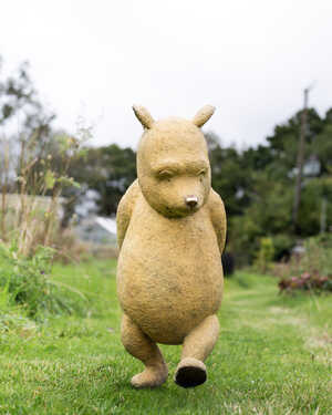 Winnie the Pooh sculpture that captures the bear walking on green grass in a garden.