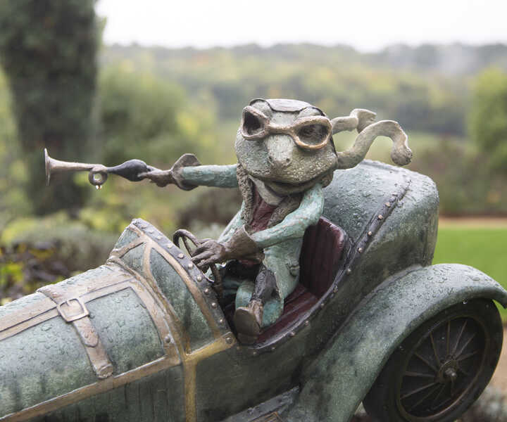 toad of toad hall garden sculpture - Mr. Toad sits in his motor car, wearing goggles, honking the horn